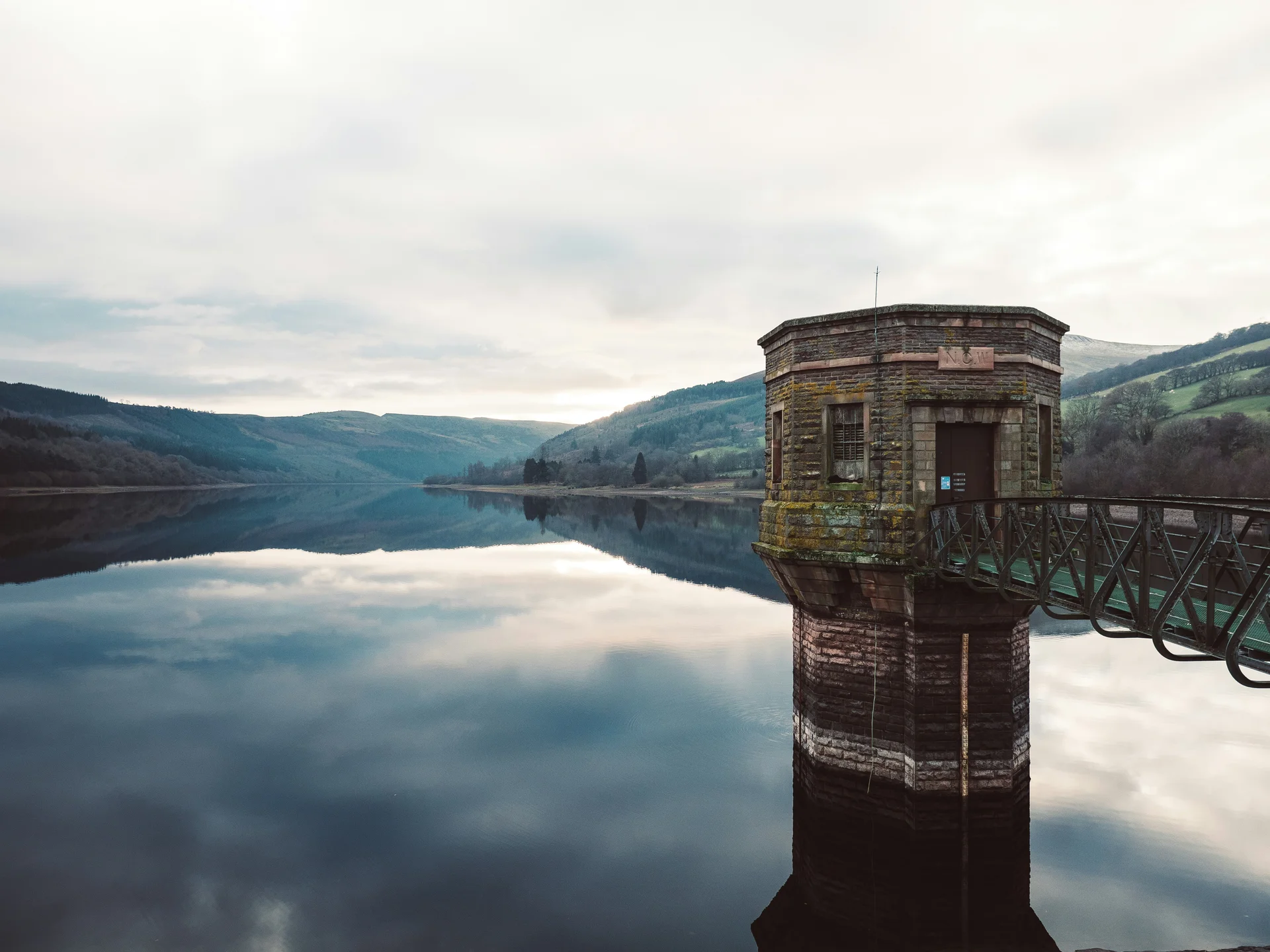 A valve tower rising from the still, mirror-flat water of Usk Reservoir