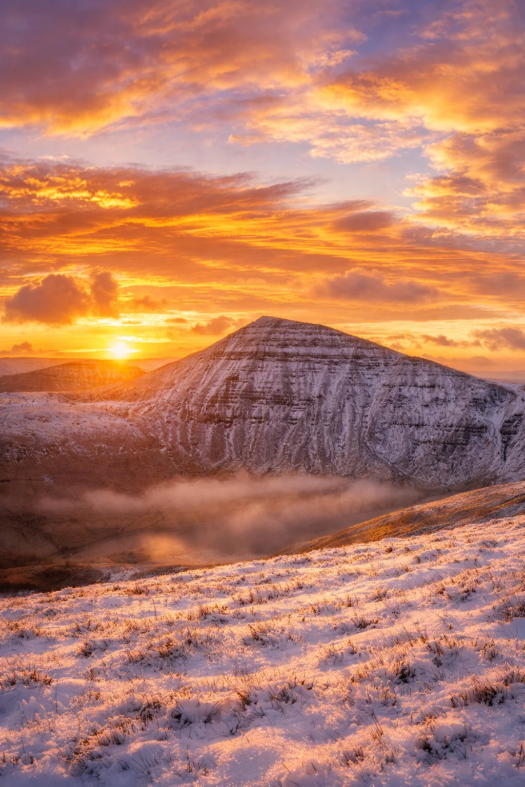The winter sun rising behind a snow-dusted Pen y Fan under orange cloud