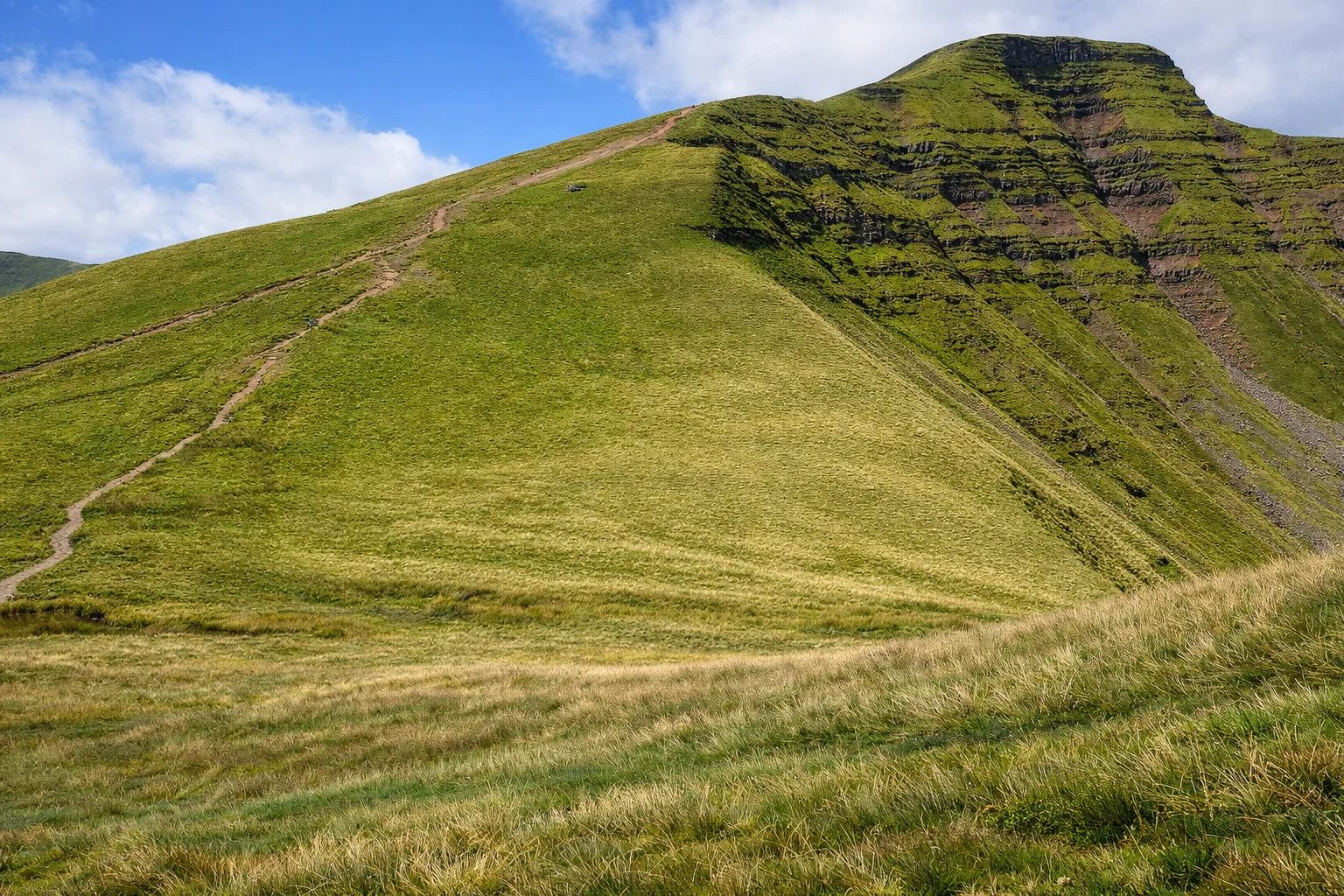 A grassy path climbing the green flank of Corn Du under a bright blue sky