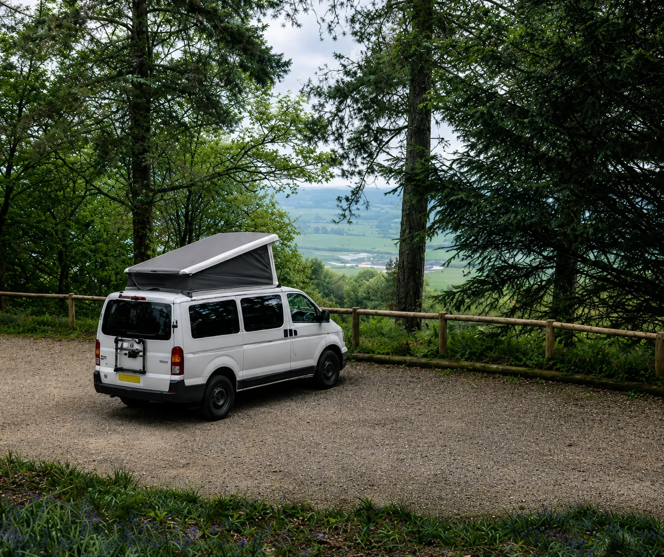A campervan parked in a forest car park with a view out over the valley