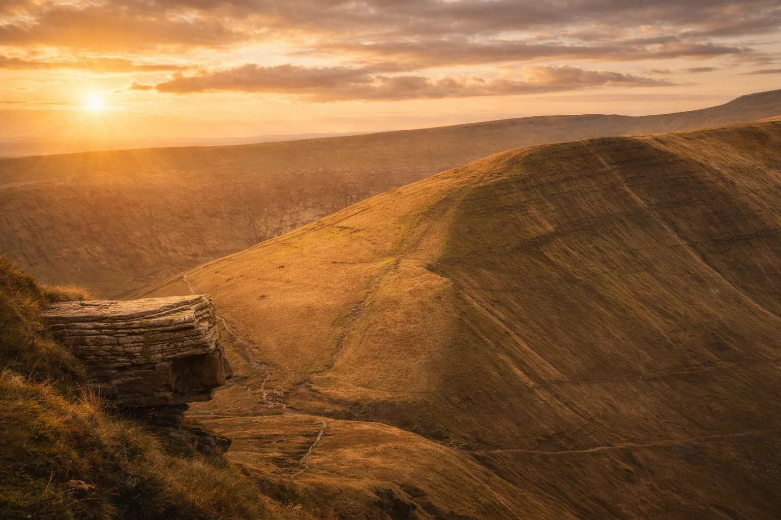 The sun setting behind a broad brown hillside in the Beacons